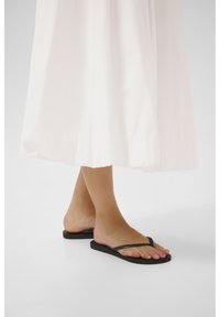 Tongs noires avec une semelle en caoutchouc lisse et des fines brides. Les brides présentent un motif texturé subtil.