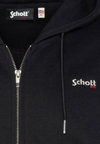 Sort zip-up hoodie lavet af bomuld med en glat tekstur. Har sølvfarvet lynlås, hætte og broderet "Schott NYC" logo i hvid og rød.