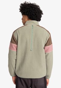 Fleece jacket in sage green, featuring brown and pink color-blocked accents, a high collar, and a centered rear zipper detail.