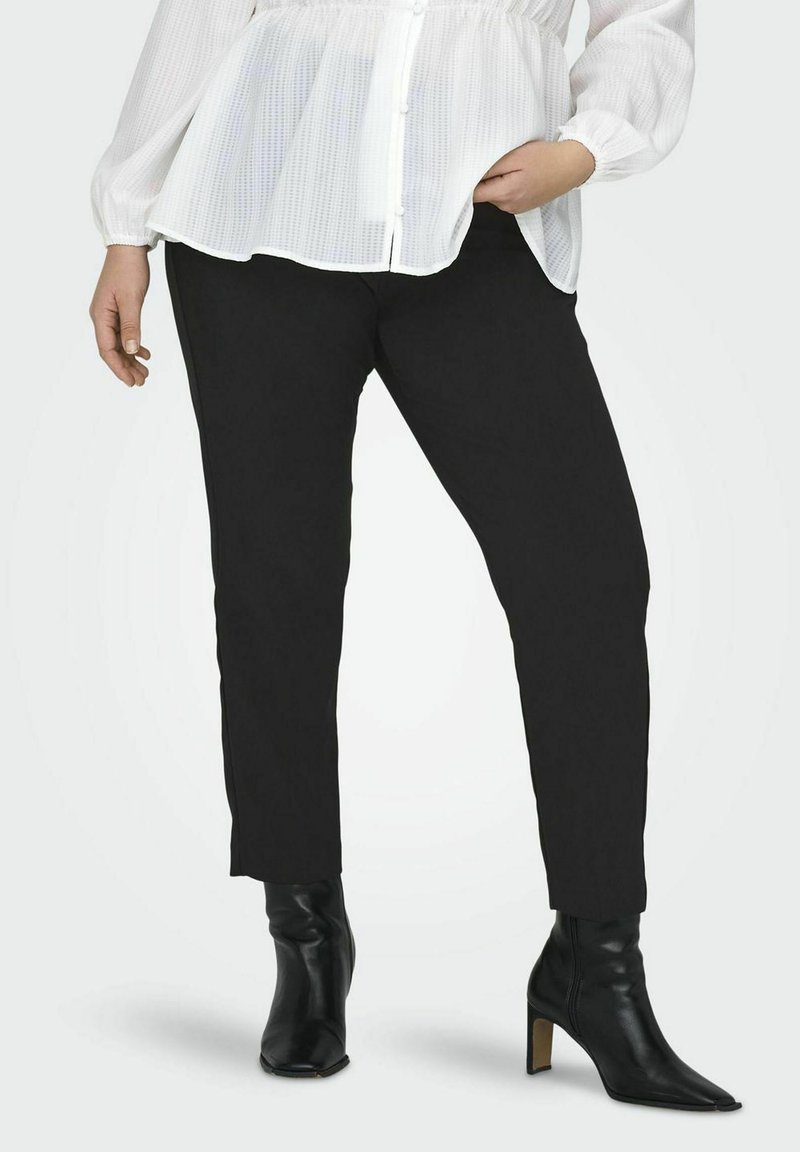 Svarta smala byxor kombinerade med en vit peplumblus med knappliknande detaljer, bäres med svarta ankelboots med spetsig tå.