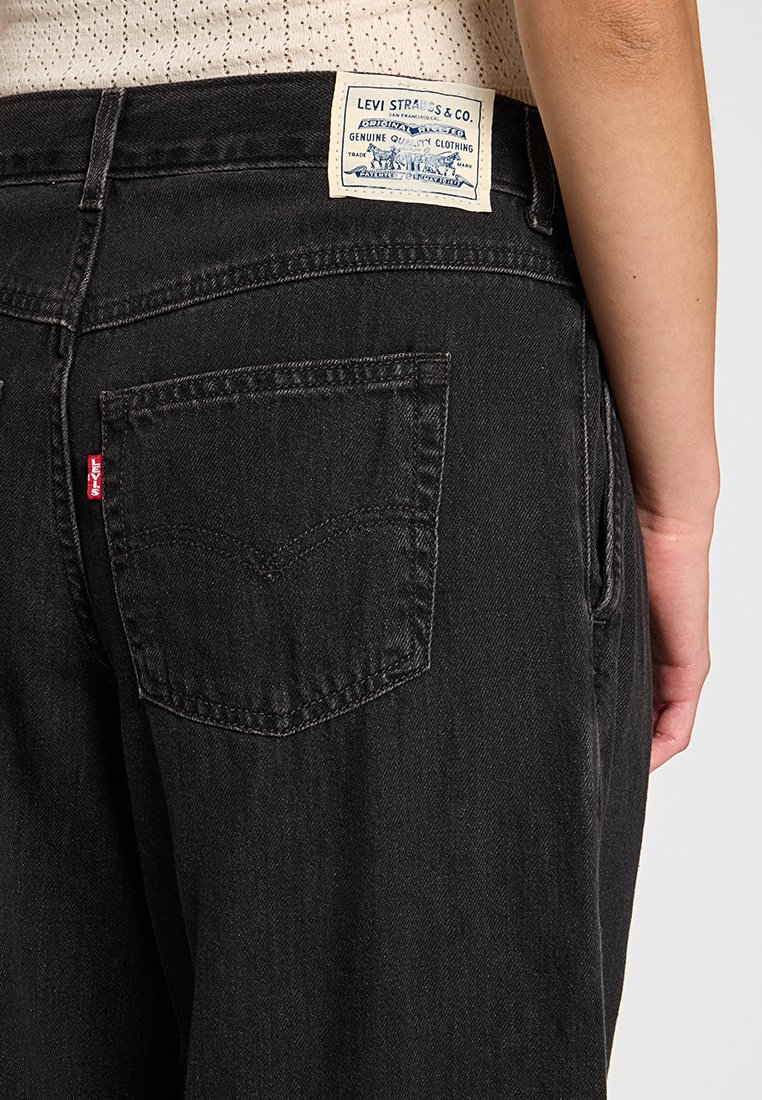 Jean en denim noir avec une poche arrière ornée de l'emblématique étiquette rouge de Levi's et d'une étiquette en cuir classique avec du texte bleu.