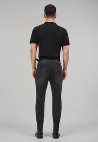 Crna polo majica u kombinaciji s tamnosivim slim-fit trapericama. Tkanina izgleda glatko, s stražnjim džepovima i ravnim krojem.