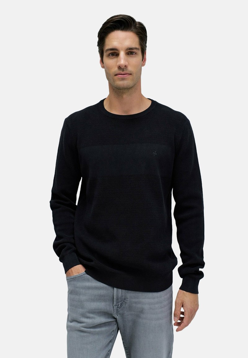 Suéter negro de punto con textura acanalada, cuello redondo y un detalle de raya horizontal. Combinado con jeans gris claro.