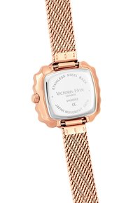 Montre en or rose avec un boîtier carré, un fond en acier inoxydable et un bracelet en maille. Le design comprend des bords arrondis et un verre transparent.