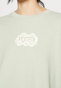 T-shirt di cotone verde chiaro con scollatura rotonda, caratterizzato da una grafica del logo Levi's bianco a forma di nuvola stampata sul petto.