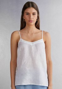 Witte linnen cami met dunne bandjes en een V-halslijn. Lichtgewicht textuur, minimalistisch ontwerp, lichte glans op de accenten van de halslijn.