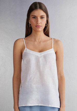 Bílý lněný top na ramínka s tenkými pásky a výstřihem ve tvaru V. Lehké potažení, minimalistický design, mírný lesk na okrajích výstřihu.