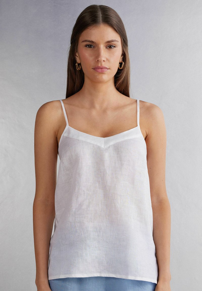 Witte linnen cami met dunne bandjes en een V-halslijn. Lichtgewicht textuur, minimalistisch ontwerp, lichte glans op de accenten van de halslijn.