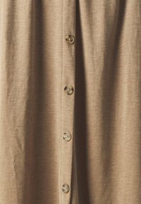 Camicia button-up in tessuto beige chiaro con una morbida texture. Presenta diversi bottoni frontali e una vestibilità rilassata. Design semplice.