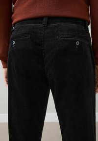 Black corduroy trousers with vertical ribbed texture, featuring two back pockets with blue buttons and a sturdy waistband.