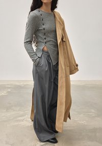 Grijze ribbed longsleeve top met zijknopen, gecombineerd met losse grijze broek en een beige jas van een gladde textuur.
