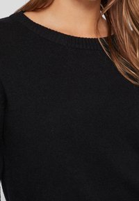 Czarny sweter z dzianiny z ribbowanym okrągłym dekoltem. Tkanina wydaje się miękka o drobnej strukturze, podkreślając jej prostotę i wszechstronność.