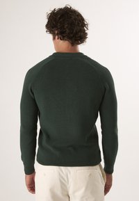 Dunkelgrüner Pullover mit gerippter Textur, langen Ärmeln und Rundhalsauschnitt. Die Rückseite verfügt über Raglanärmel für zusätzlichen Komfort und eine gute Passform.