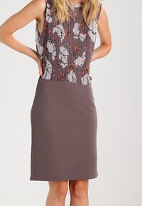 Hihaton yläpaita harmaasta kuviollisesta kankaasta, jossa on oransseja kukkakuvioita, yhdistettynä hyvin istuvaan ruskeaan kynähameeseen. Pehmeä tekstuuri ja yksinkertainen siluetti.