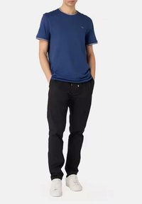 T-shirt blu navy a maniche corte con colletto e polsini a contrasto, abbinato a pantaloni jogger neri e sneakers bianche.