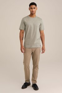 Gaiši pelēka, īsām piedurknēm T-kreklu ar apaļu kakla izgriezumu, saskaņots ar bēšām biksēm un melniem šņorējamiem apaviem. Abi apģērba gabali ir neformāla stila.