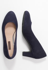 Chaussures à talons hauts en daim bleu marine avec un bout pointu et une surface texturée. Dispose d'un talon en caoutchouc noir et d'une semelle intérieure rembourrée avec un logo.