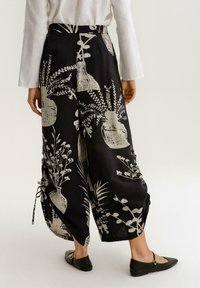 Černé široké kalhoty s bílými vzory květinových váz, volný střih a stahovací prvky na lemu. Lehce materiál.