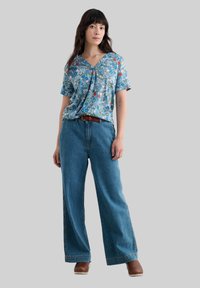 T-shirt à manches courtes et décolleté en V à motif floral, de couleur bleu clair ; associé à un pantalon en denim bleu à coupe ample et des sabots marron. Il présente une ceinture tissée.