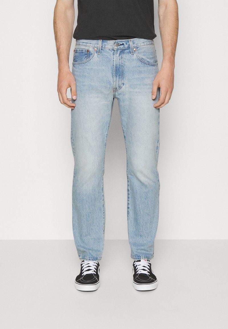 Jean en denim bleu clair avec une coupe droite, un design à cinq poches et une texture délavée. Associé à des baskets noires et un t-shirt noir.