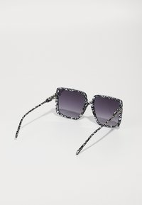 Square sunglasses with a black and white patterned frame, dark gradient lenses, and slender patterned arms.
