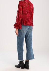Rød blondebluse med lange ærmer og volantsøm, parret med bleget blå cropped jeans. Sorte ankelstøvler fuldender outfittet.