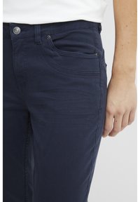 Sötétkék pamut elasztikus nadrágok elülső zsebekkel, slim fit szabásban és sima textúrával. Ezüst színű fém gombbal és szegecsekkel rendelkezik.