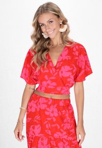 Top corto floreale rosso con design avvolgente, maniche corte e gonna coordinata con volant. Il tessuto ha una superficie liscia e motivi rosa audaci.
