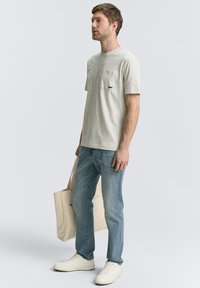 Tricou scurt alb-gri cu mâneci scurte și buzunar pe piept, asortat cu blugi albaștri deschiși și adidași albi, purtând o geantă tote bej.