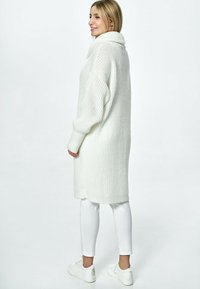 Biały, oversize'owy sweter z dzianiny z dekoltem typu cowl, długimi rękawami i prążkowanymi mankietami. Połączony z białymi rurkami i białymi sneakersami.