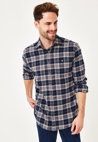 Marineblaue Karobluse mit weißen und braunen Linien, Knopfverschluss vorne und hochgekrempelten Ärmeln, aus einem weichen Stoff gefertigt. Mit kleiner Brusttasche.