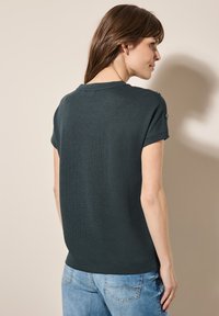 Tmavě šedý svetr s krátkým rukávem a texturovaným pletením, se dvěma knoflíky na každém rameni a designem s kulatým výstřihem.