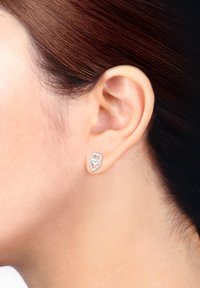 Silberne Ohrringe im Doppelherzdesign. Sie verfügen über eine glänzende Oberfläche und eine glatte Textur und sind am Ohrläppchen befestigt.