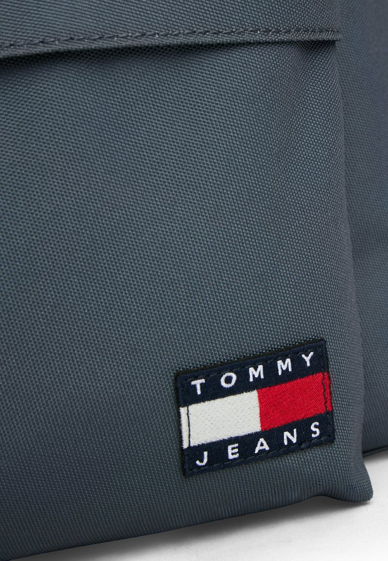 Gray fabric, smooth texture, featuring a rectangular patch with "TOMMY JEANS" in white on blue, red, and white stripes.