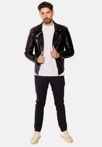 Svart läderbikerjacka med kviltade detaljer, vit t-shirt, mörka jeans och krämfärgade sneakers. Modellen står med tummarna upp.