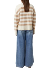 Sweter dzianinowy w kremowo-beżowe paski o luźnym kroju, zestawiony z szerokimi dżinsami o wysokim stanie w jasnym odcieniu niebieskiego.