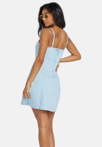 Hellblaues Denim-Kleid mit dünnen Trägern, tailliertem Oberteil und schwingendem Rock, ausgestattet mit einem seitlichen Reißverschluss und minimalen Nähdetails.