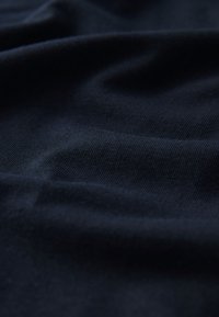 Dunkel marineblaues Gewebe mit einer glatten, strukturierten Oberfläche, die subtile Falten und Knicke aufweist, wodurch die weiche, dehnbare Qualität betont wird.