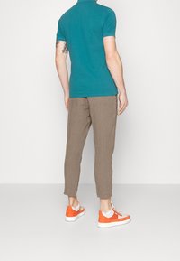 Teal polo shirt, ljusbruna tapered byxor, vita och orange sneakers. Tyget ser slätt ut, med en figursydd design och korta ärmar.