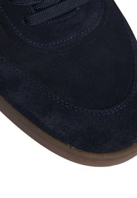 Navy blue suede sneaker with textured surface, round toe, and light brown rubber sole. Features navy laces and contrasting stitching details.