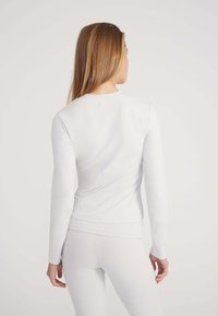 Langärmeliges weißes Oberteil aus weichstoff, mit rundem Ausschnitt und figurbetonter Passform. Nahtloser Rücken und Bündchen mit dezentem Stitching.