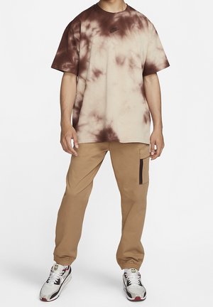 Tie-Dye-T-Shirt in Beige und Braun, mit Rundhalsausschnitt und kurzen Ärmeln. Kombiniert mit khakifarbenen Cargo-Hosen und weißen Sneakers mit Akzenten.