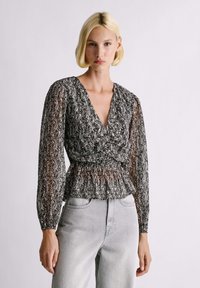 Čiernobiela blúzka so vzorom, s dlhými, priehľadnými rukávmi a hlbokým výstrihom do V. Má zoštíhľujúci pás s nariasením a voľný peplumový spodok.