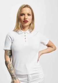 Hvit ribbestrikket poloshirt med korte ermer og krage, med tre dekorative knapper. Jevn tekstur og tettsittende design.