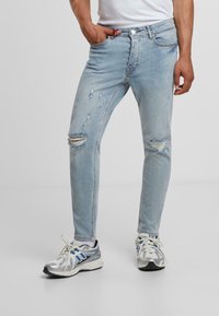 Fénykék, slim-fit farmernadrág, térdén kivágott és kopott hatással. Az anyag lágy érzetű; standard zsebekkel és öt övhurkkal rendelkezik.