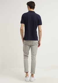 Granatowa koszulka polo z klasycznym kołnierzykiem, zestawiona z jasnoszarymi spodniami slim-fit i białymi trampkami, widok od tyłu.