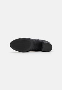 Vista inferior de un zapato negro con una suela texturizada y un talón suave, mostrando su diseño y patrón de agarre.