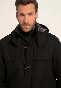 Abrigo de mezcla de lana negra con cierres de toggles, un cuello alto y un forro interior de cuadros. Presenta un diseño estructurado y una textura suave.