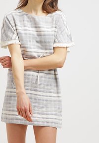 Raidallinen vaaleanvärinen mekko, jossa on lyhyet hihat, teksturoitu kangas, naru vyötäröllä ja frangeja hihoissa.