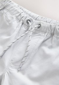 Primo piano dei pantaloncini con fascia elastica bianca e coulisse bianca e nera legata attraverso occhielli metallici.